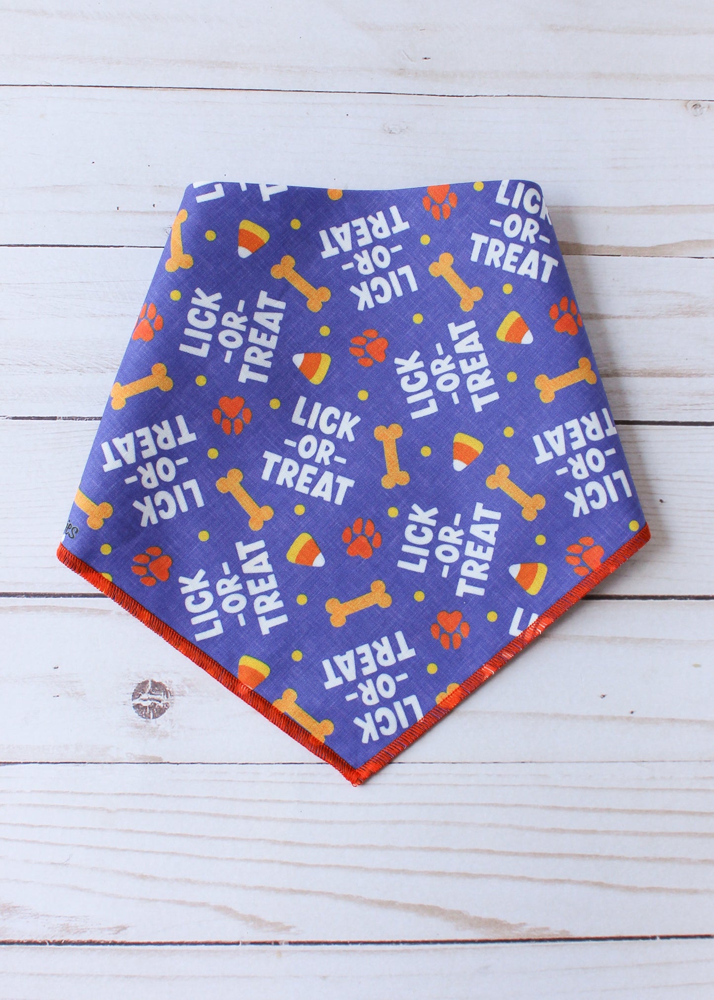 Dog bandana with 'Lick or Treat' text and bone designs on a white wooden surface