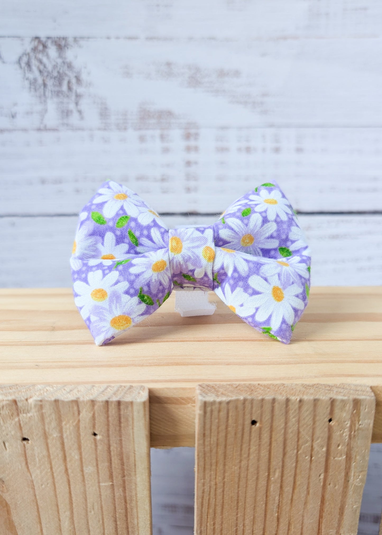 purple daisy dog bow on a wooden surface with a light gray background