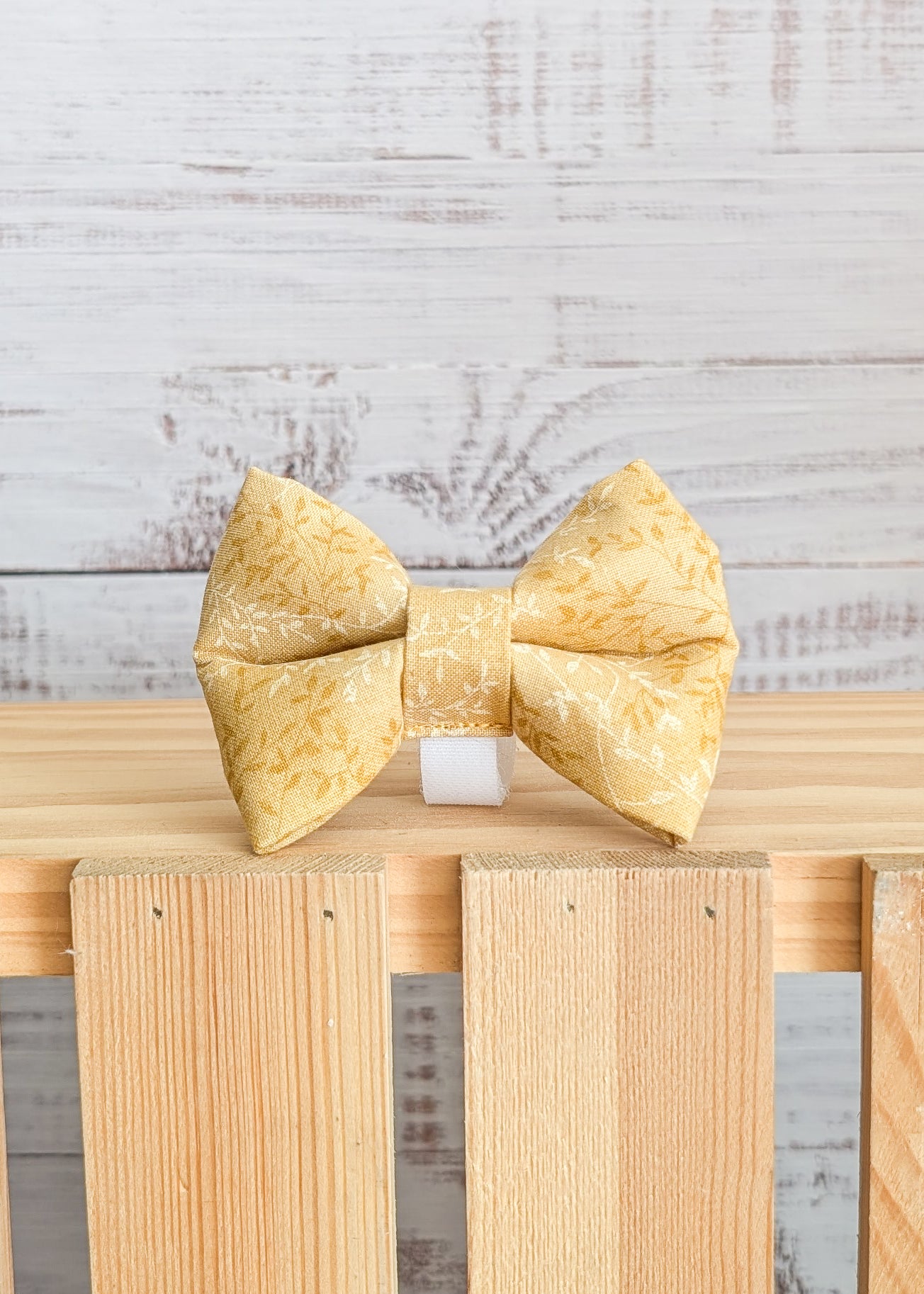 light yellow bow tie with a light leaf pattern on a wooden block with a light gray background
