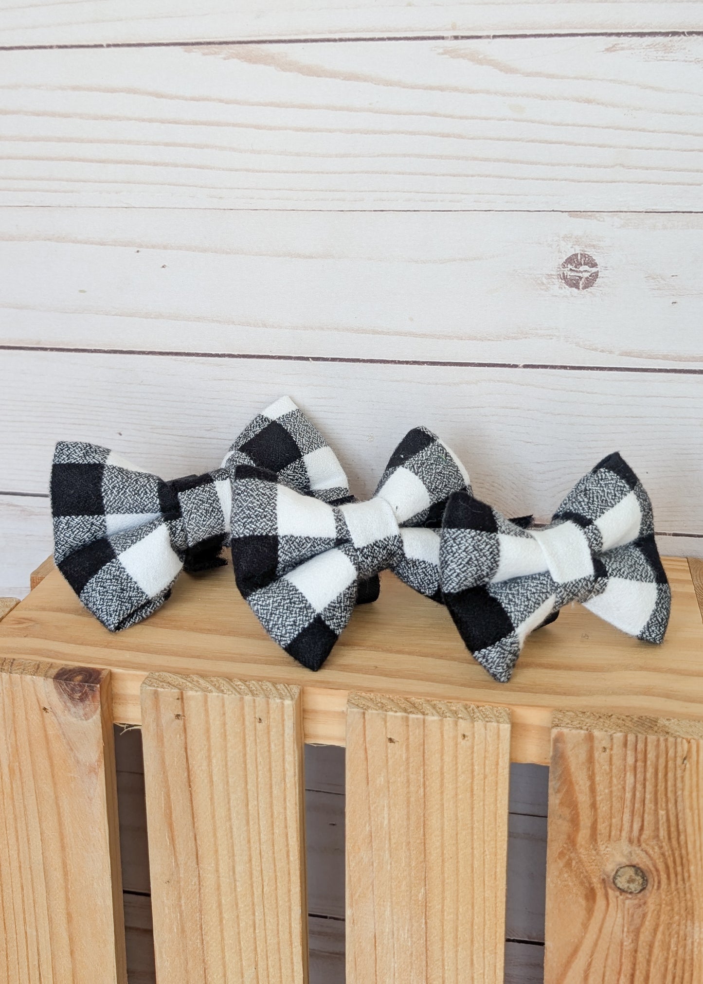 Three black and white buffalo plaid bow ties arranged on a wooden crate against a light wood plank background.