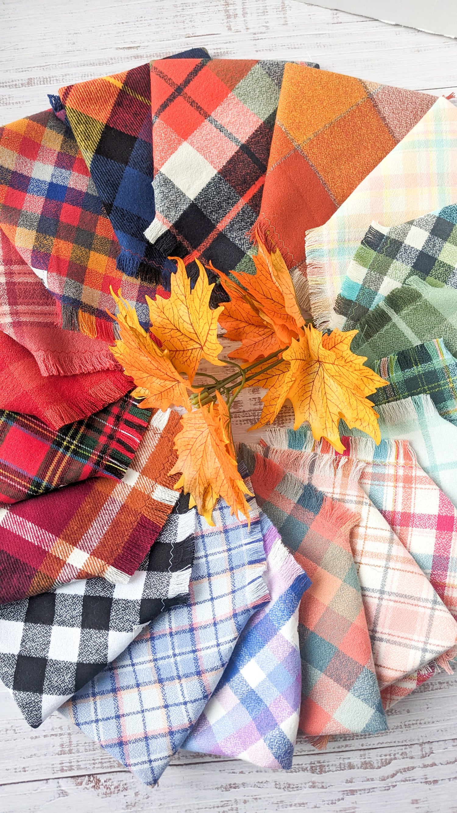 Various Flannel bandanas folded and placed in a circle pattern with maple leaves in the middle