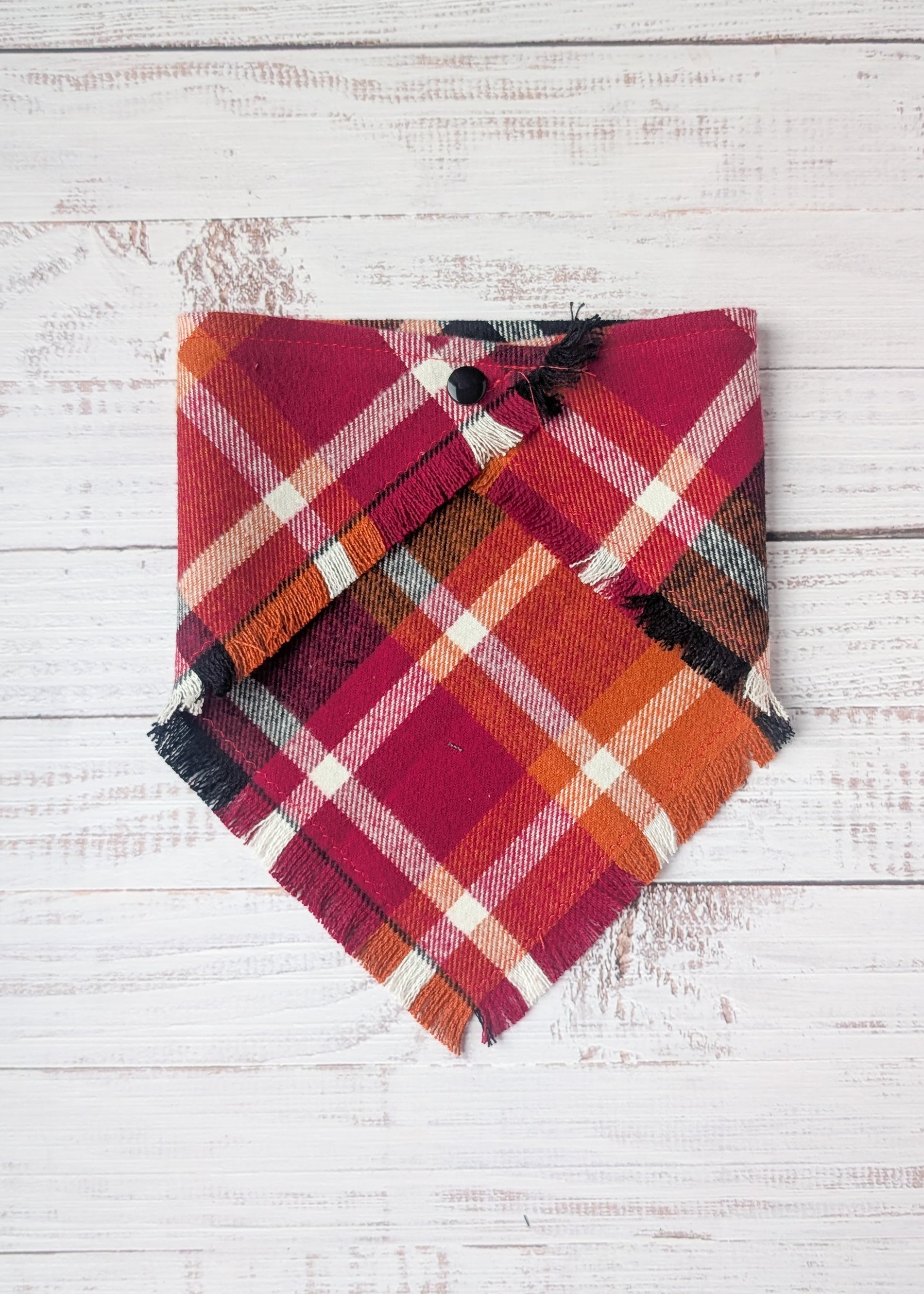 Plaid Flannel Bandana with maroon, black, orange, white plaid pattern on a wooden surface