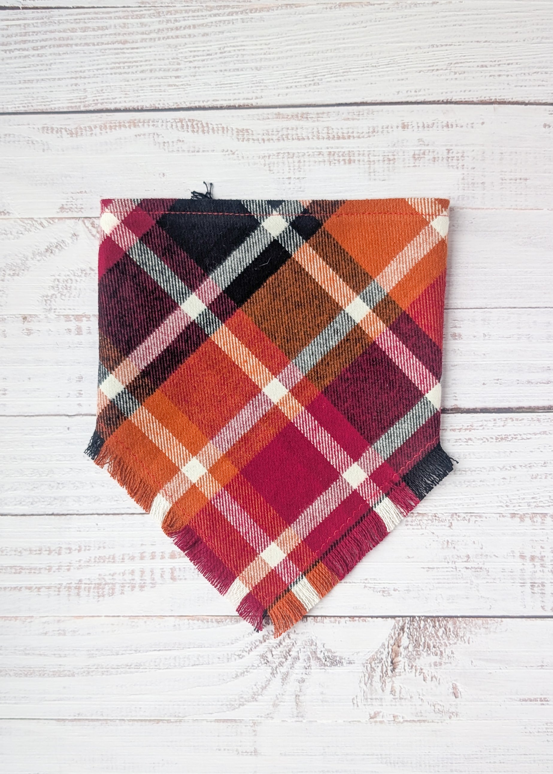 Plaid Flannel Bandna with maroon, black, orange, white plaid pattern on a wooden surface