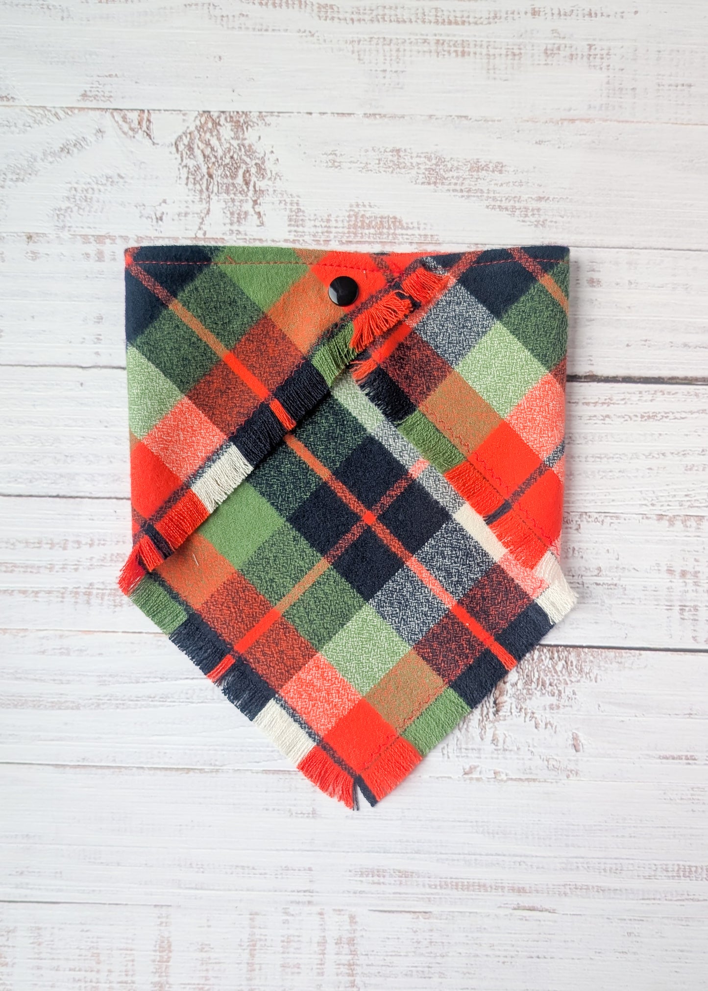 Green, Black, white, and orange plaid flannel bandana on a wooden background