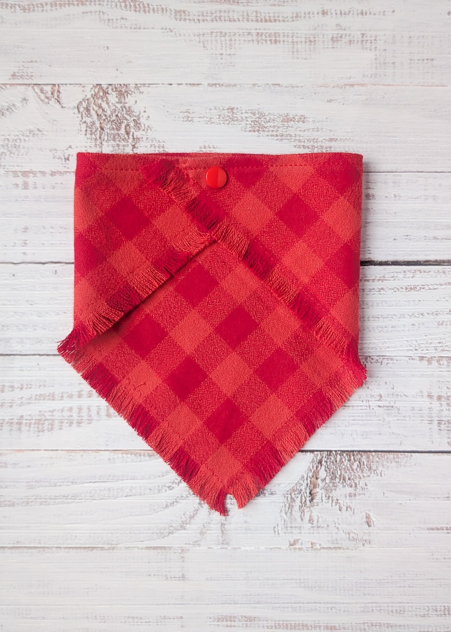 Red plaid flannel bandana with a button on a white wooden background