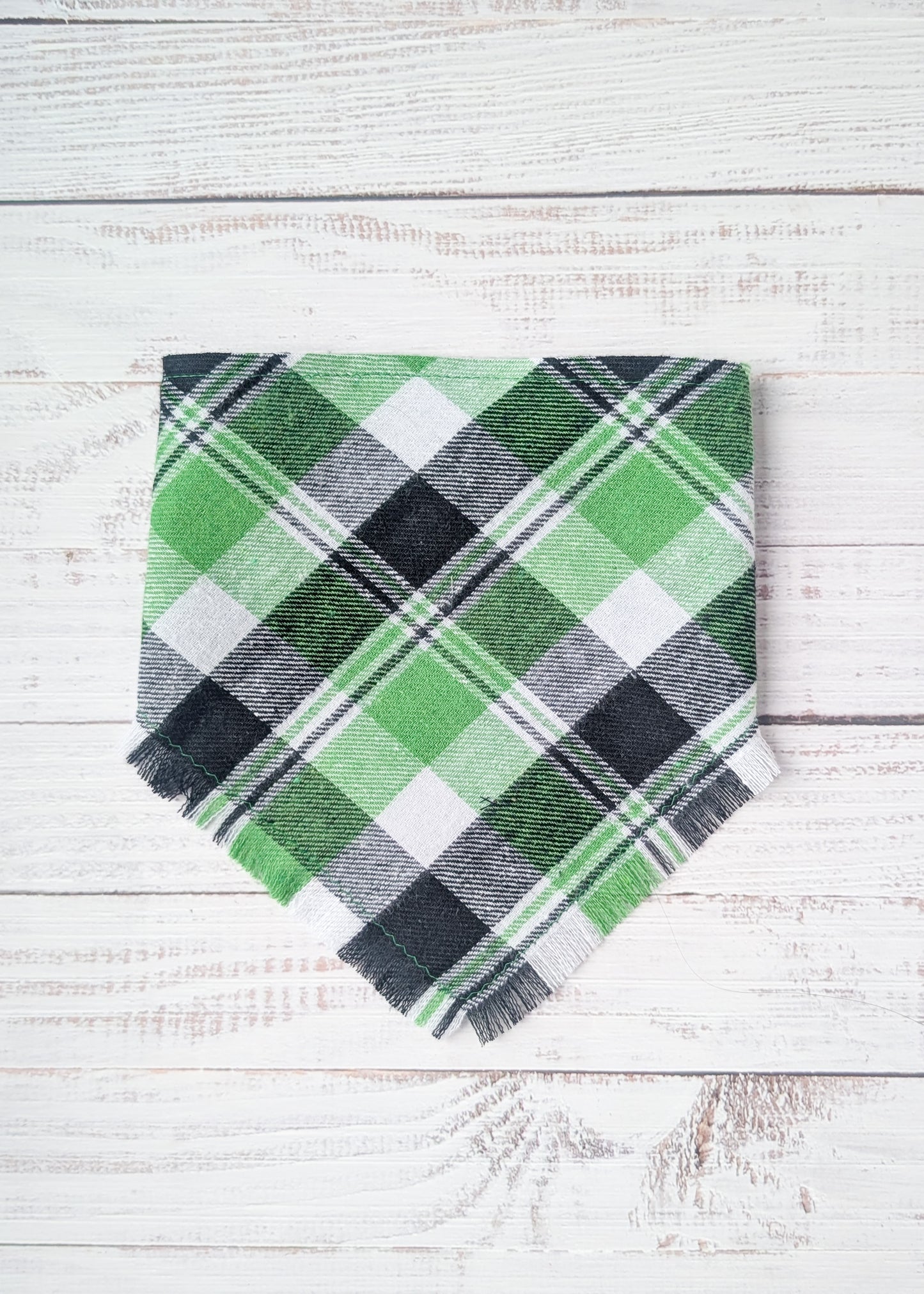 Green and black plaid flannel bandana with fringe on a white wooden surface