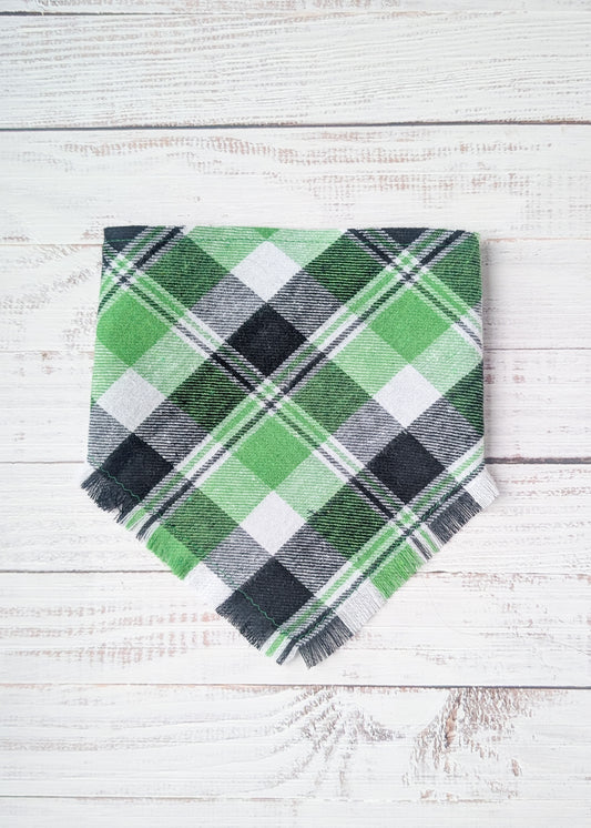Green and black plaid flannel bandana with fringe on a white wooden surface