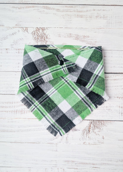Green and black plaid flannel bandana with fringe on a white wooden surface