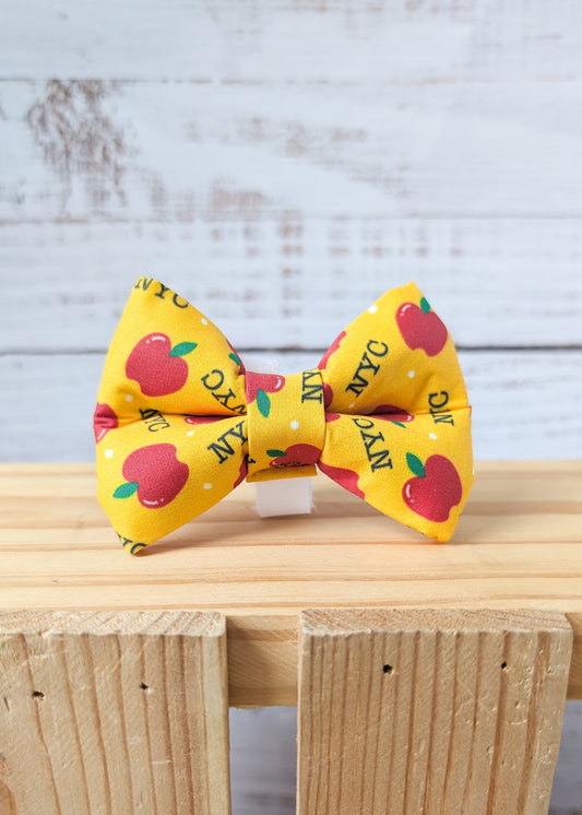 Yellow dog bow tie with red apples and "NYC" repeating pattern