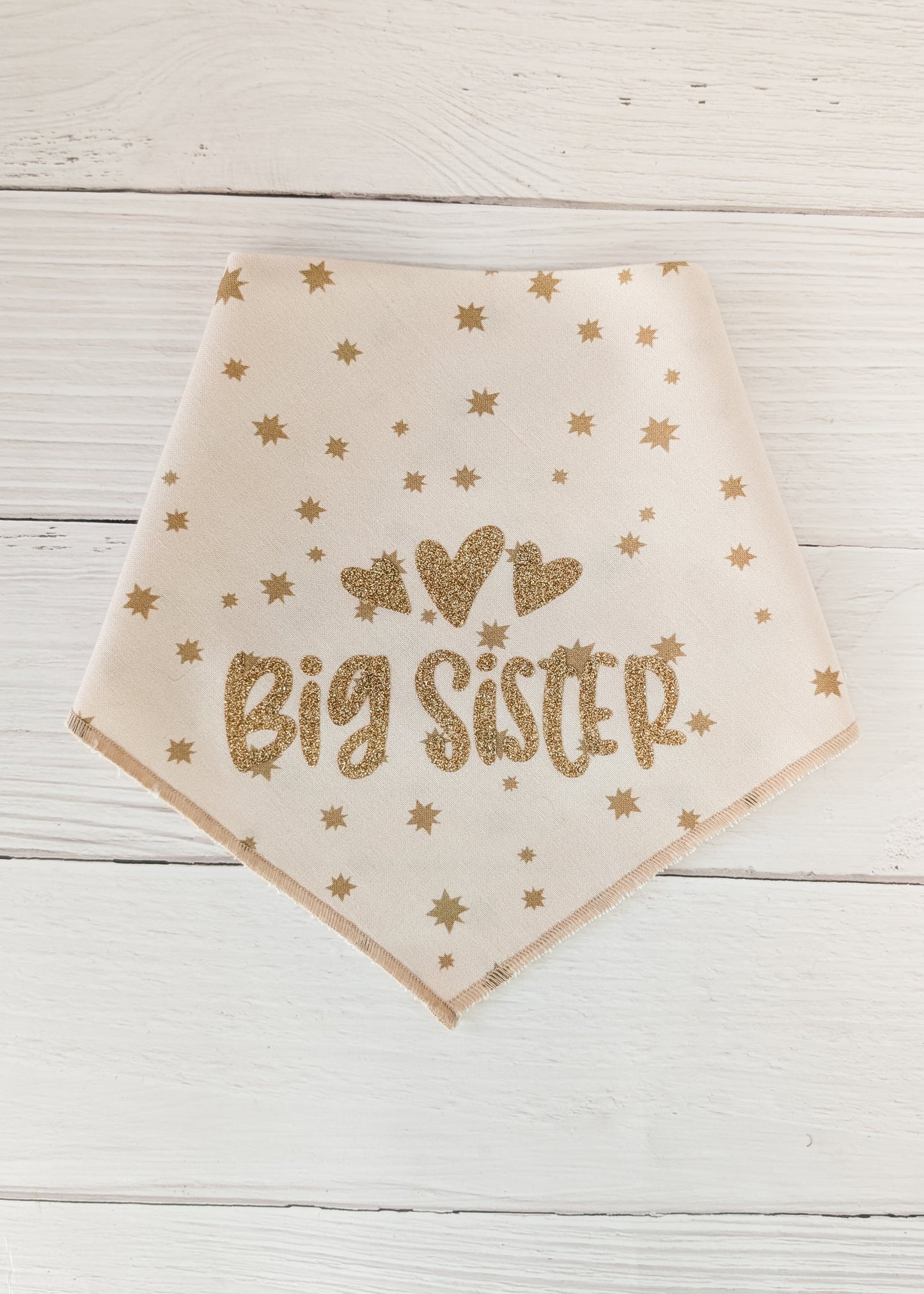 Beige bandana with 'Big Sister' text and gold hearts on a wooden surface