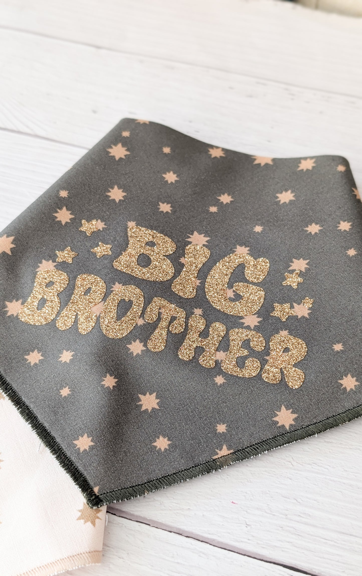 Dark Olive bandana with gold 'Big Brother' text and star patterns on a light wooden surface