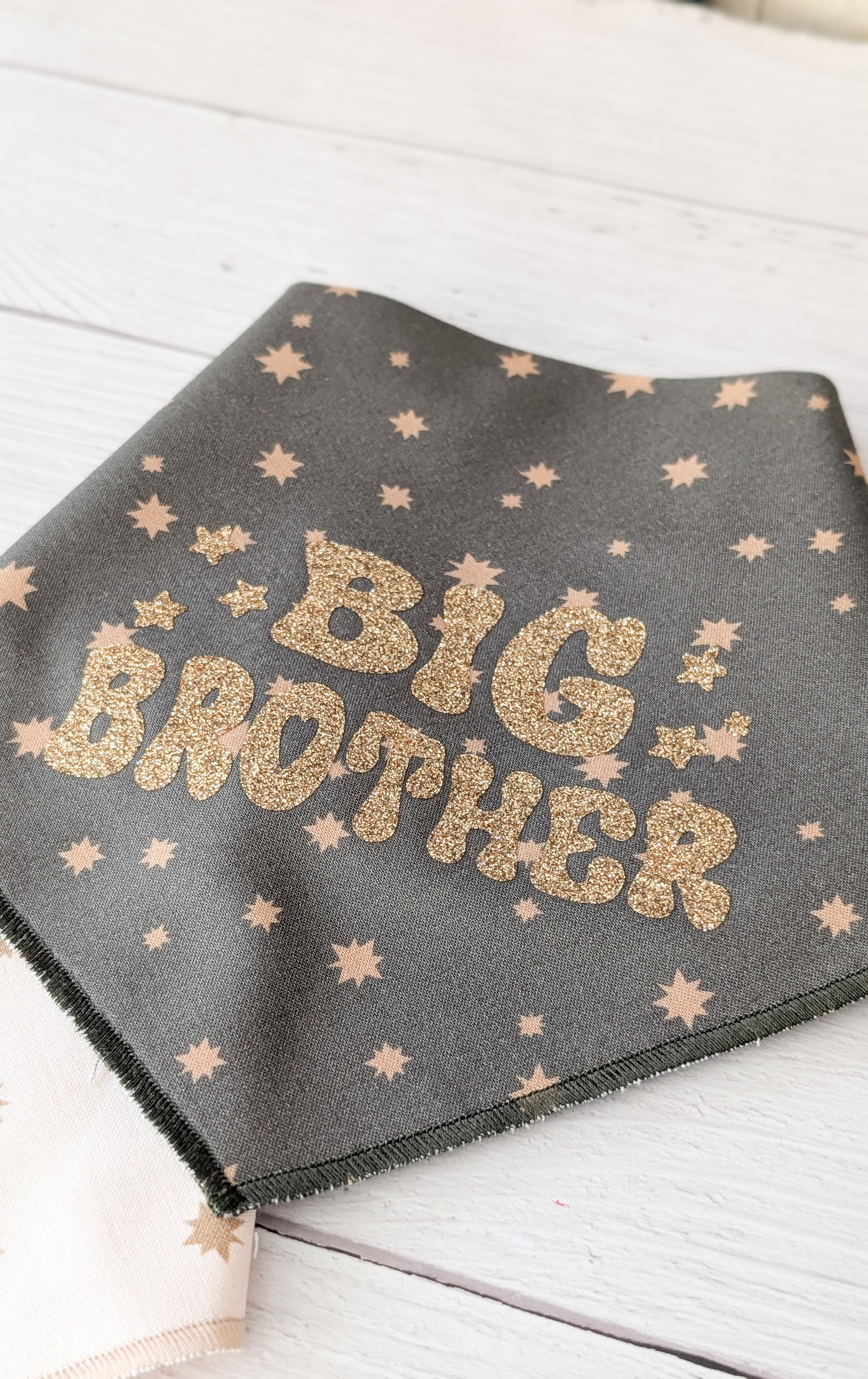 Dark Olive bandana with gold 'Big Brother' text and star patterns on a light wooden surface