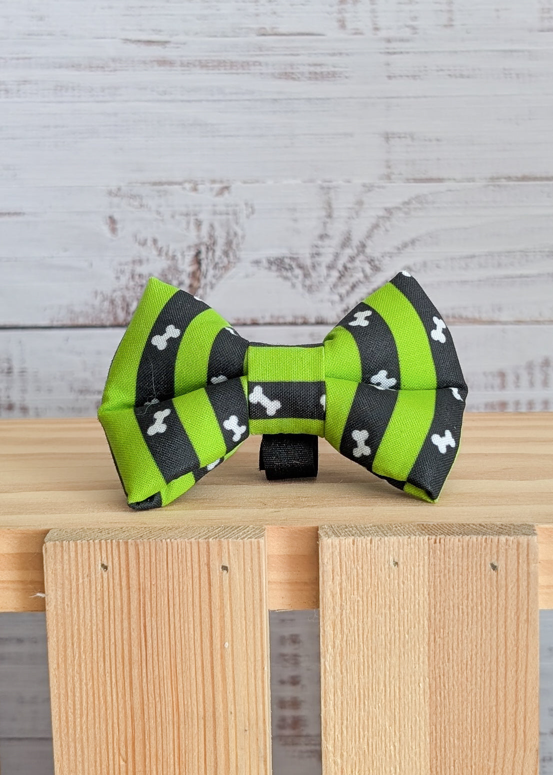 Green and black striped bow tie with bone pattern on a wooden block against a rustic wooden background