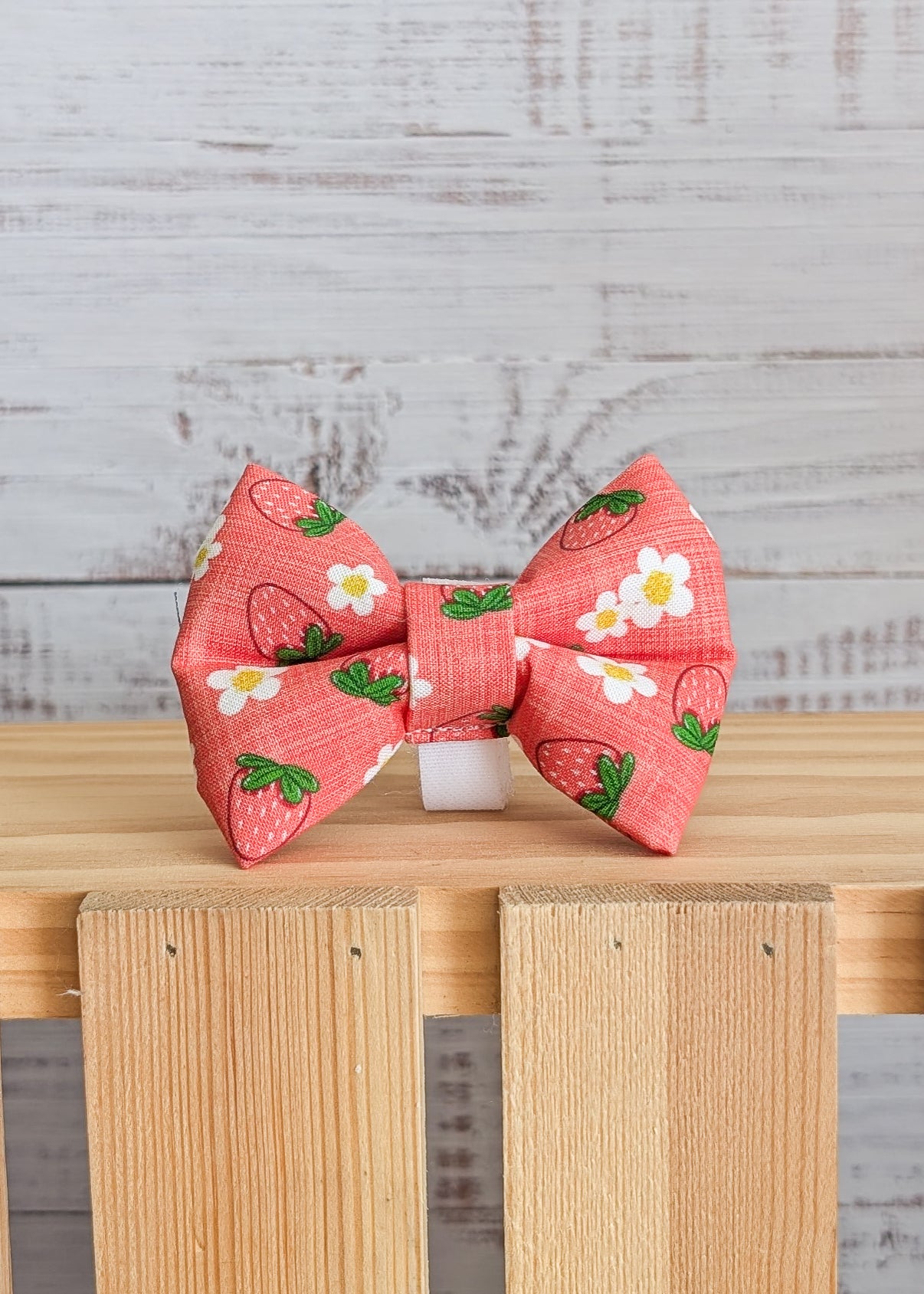 Red bow with strawberry patterns on a wooden surface and light gray background