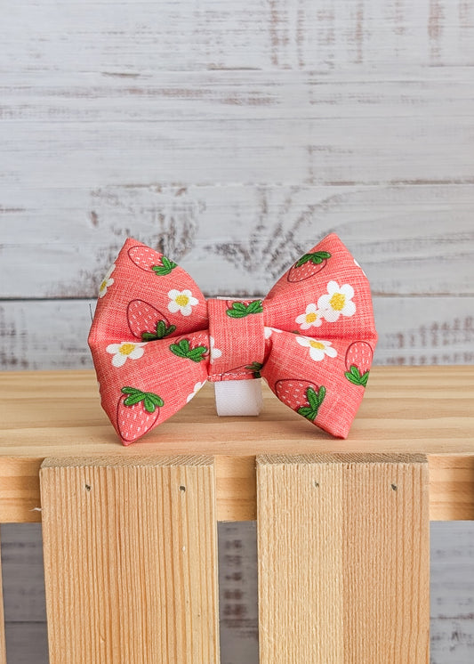 Red bow with strawberry patterns on a wooden surface and light gray background
