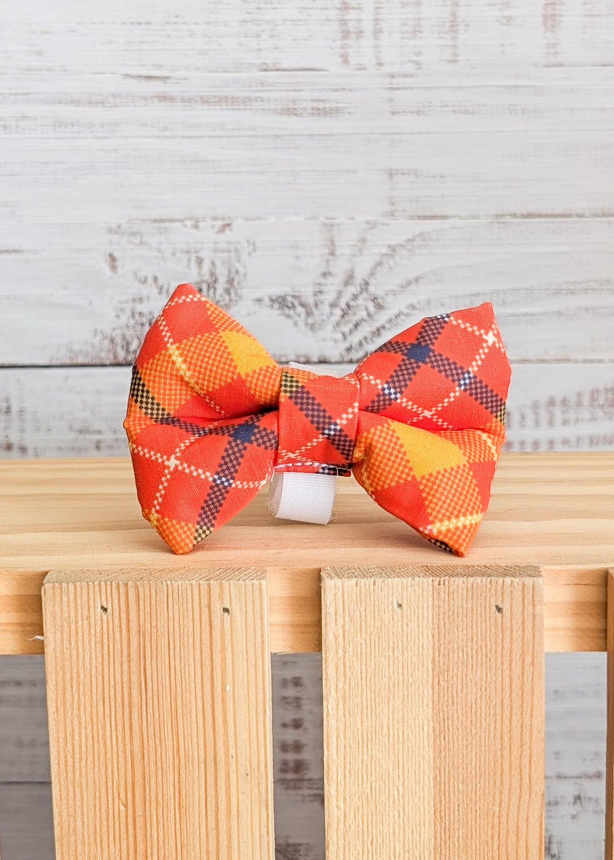 Orange plaid bow tie on a wooden stand and white wood background