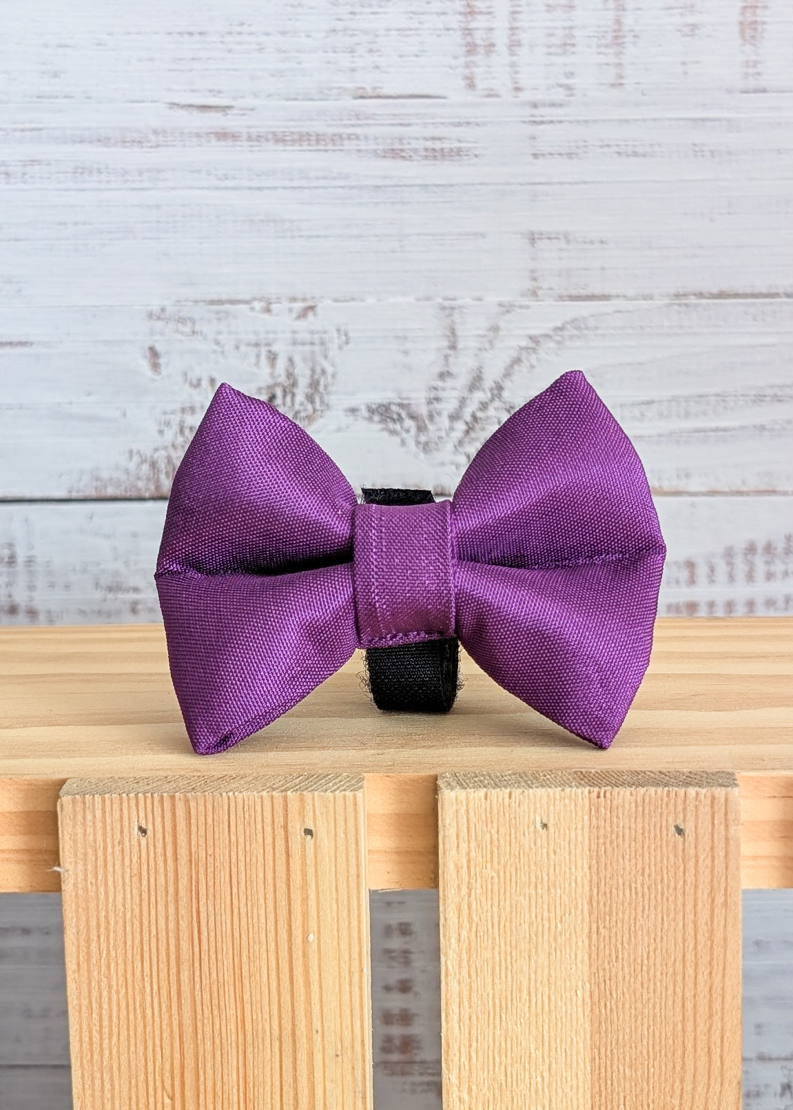 Purple bow tie on a wooden surface with a light gray background