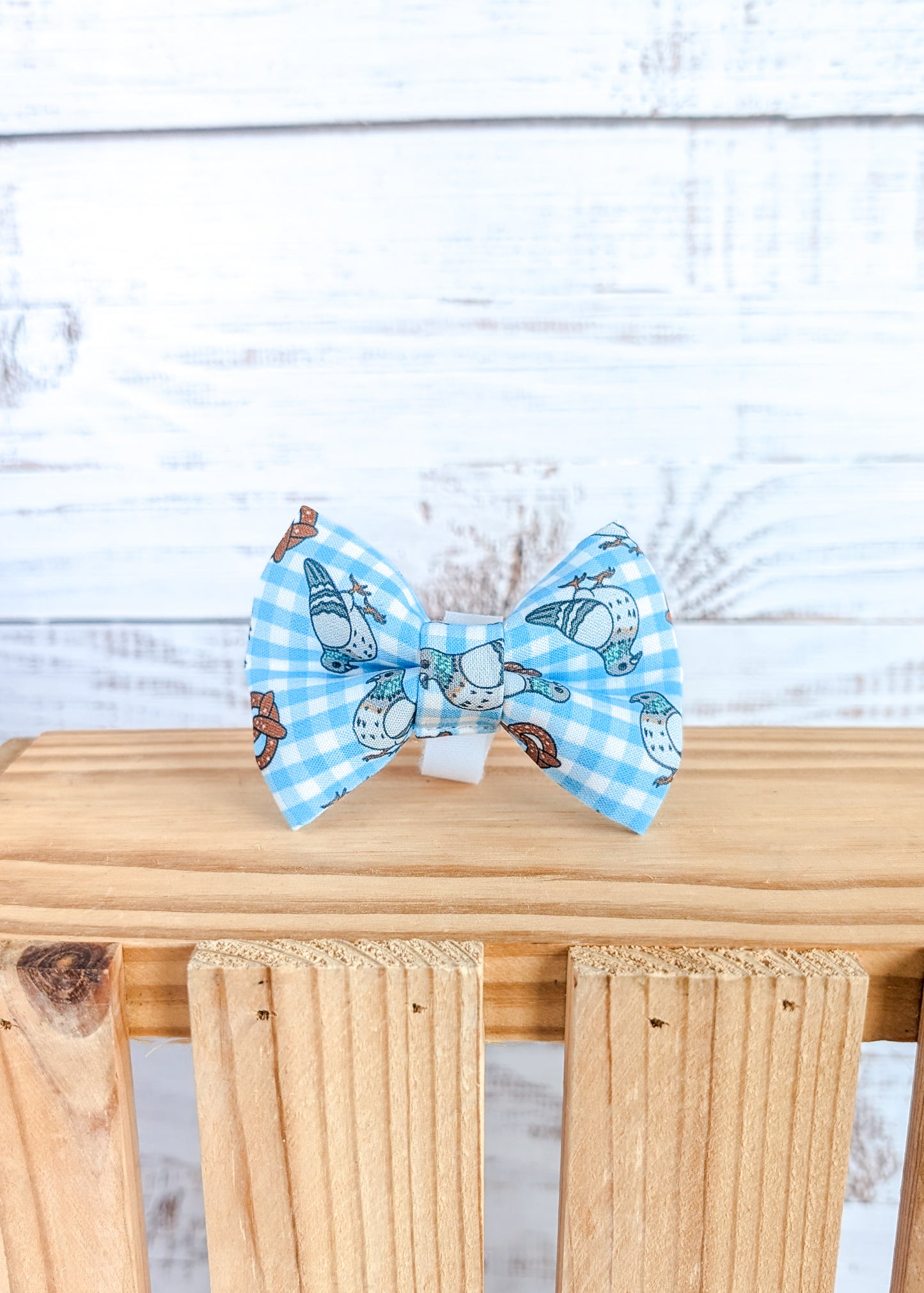 Blue checkered bow tie with pigeon and pretzel design on a wooden surface