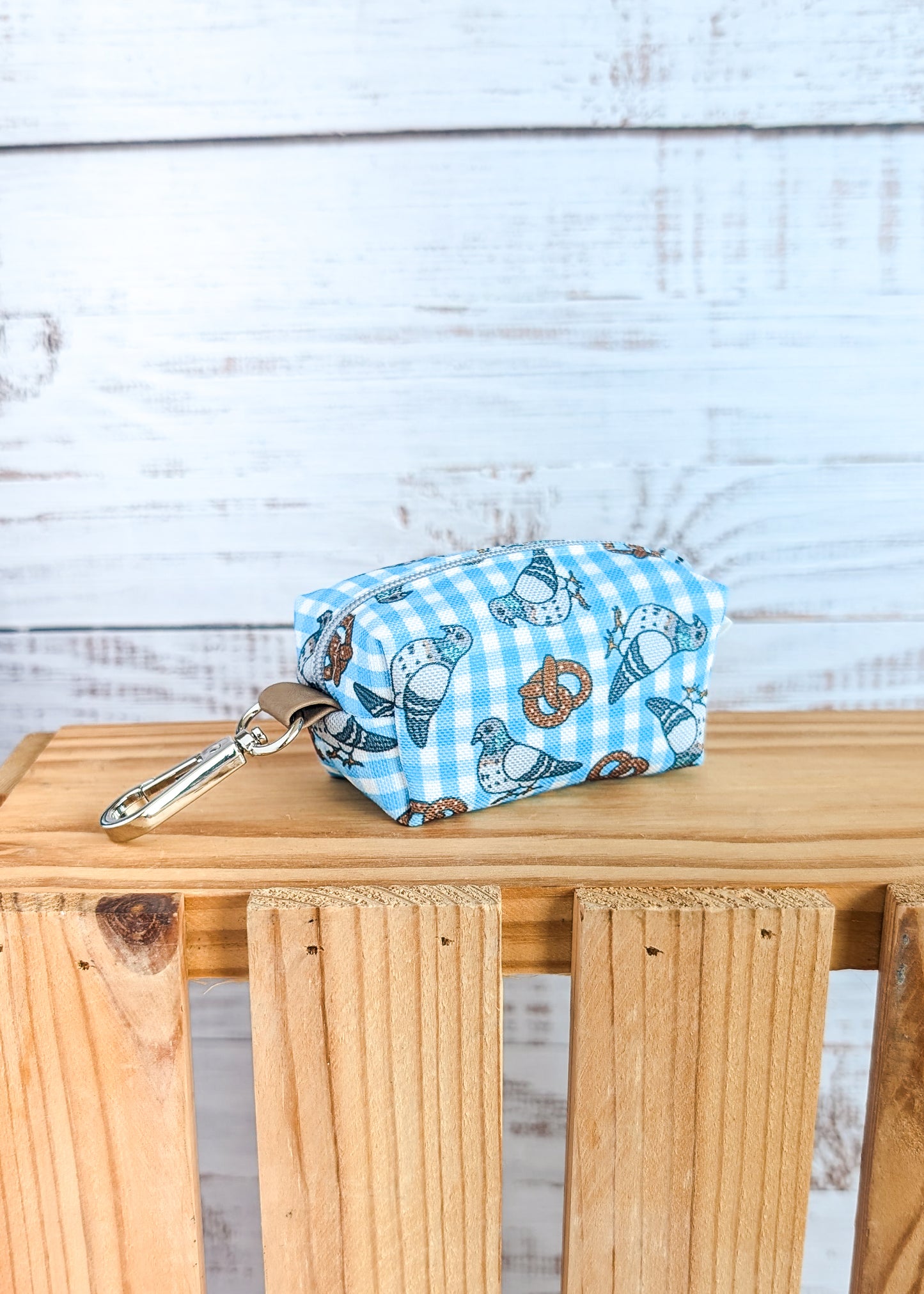 Small pouch with pigeon and pretzel design on a wooden surface against a light wooden panel background