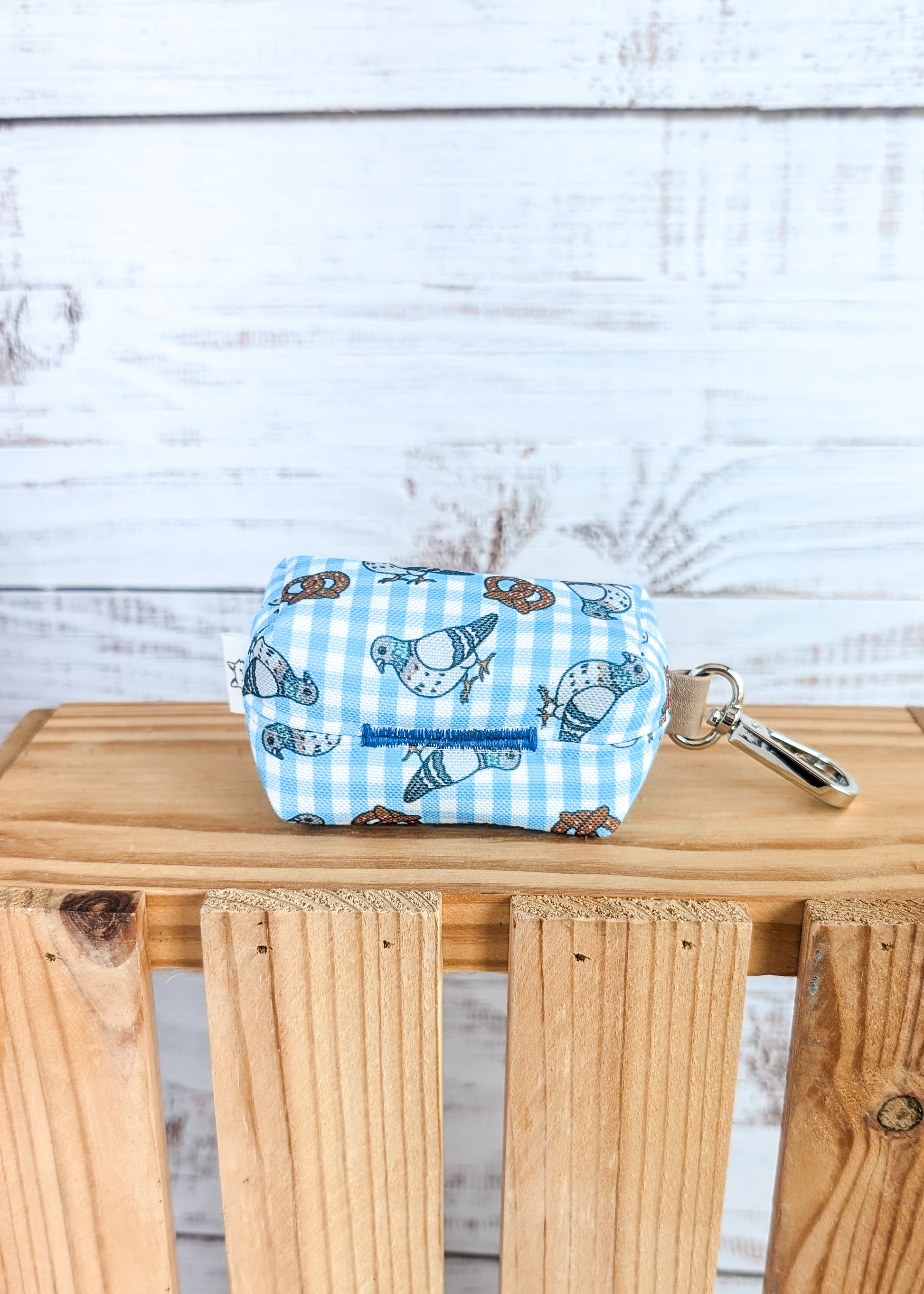 Small pouch with pigeon and pretzel design on a wooden surface against a light wooden panel background