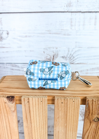 Small pouch with pigeon and pretzel design on a wooden surface against a light wooden panel background