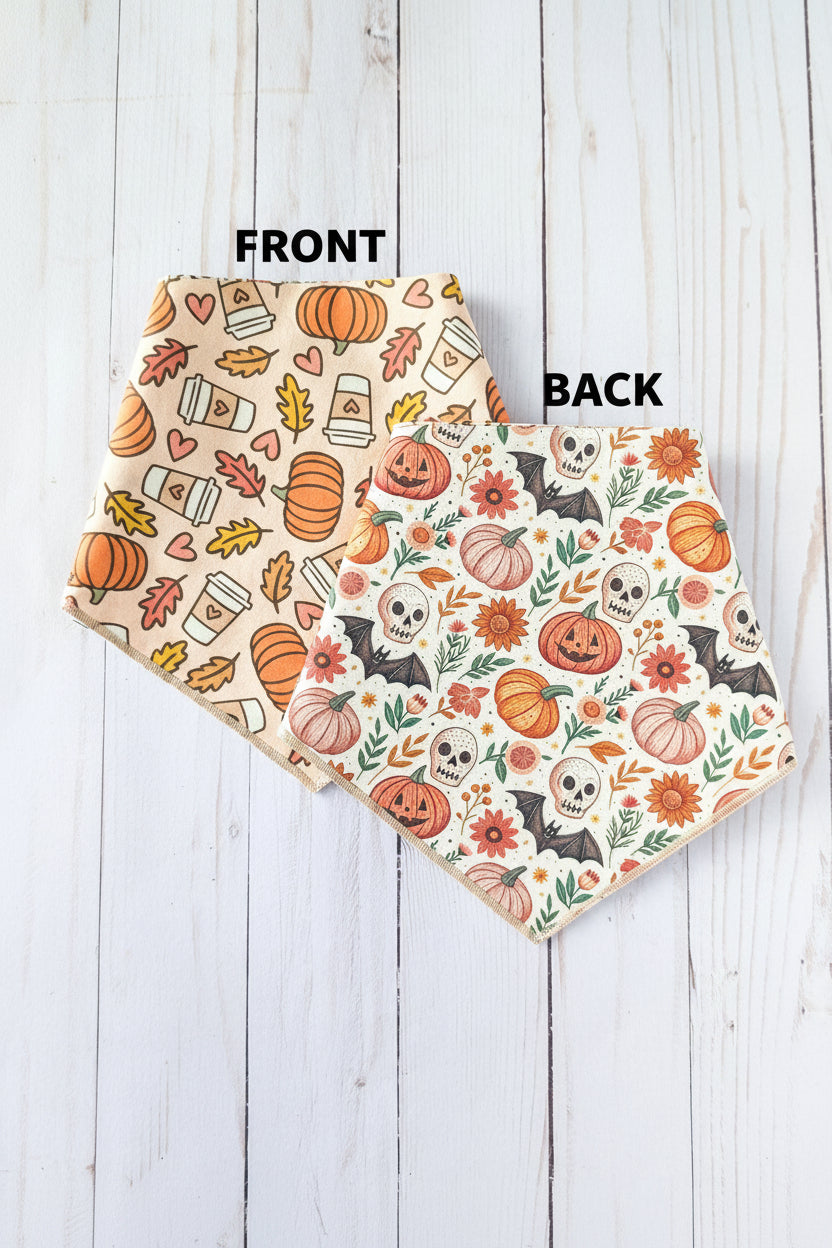 Two triangle bandanas with autumn Halloween patterns, displayed on a white wood plank background. One bandana features orange pumpkins, coffee cups, and hearts on a beige background, while the other features orange pumpkins, skulls, flowers, and bats on a white background.