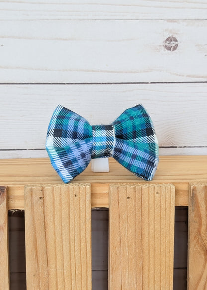 A blue and green plaid bow tie displayed on a wooden slatted surface against a white wood plank background.