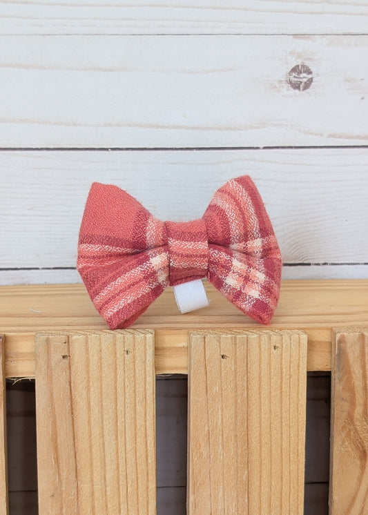 A red and pink plaid bow tie displayed on a light wood slatted surface against a white wood plank background.