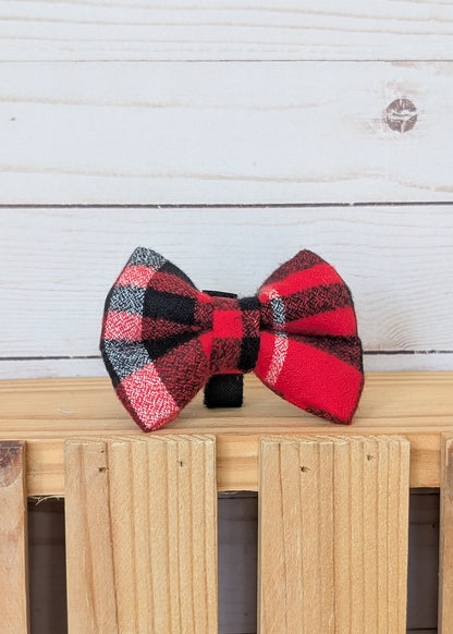 A red and black buffalo plaid bow tie displayed on a light wood slatted surface against a white wood plank background.
