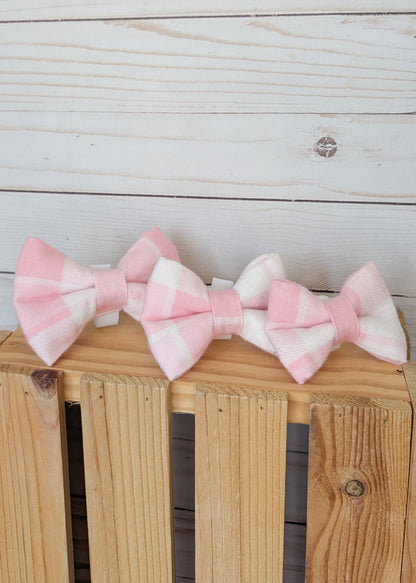Three pink and white gingham bow ties arranged on a wooden crate against a white wood plank background.
