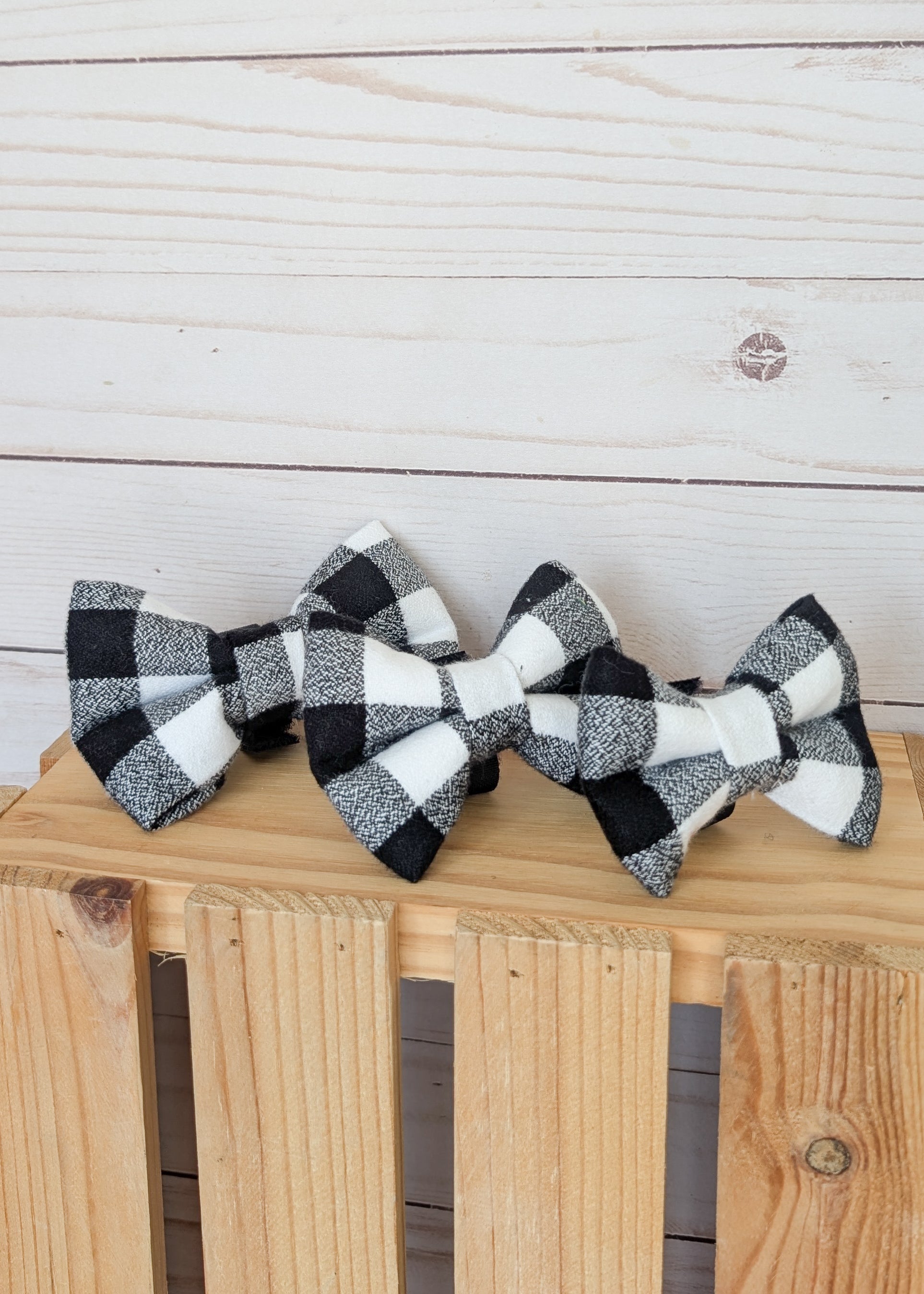 Three black and white buffalo plaid bow ties arranged on a wooden crate against a light wood plank background.