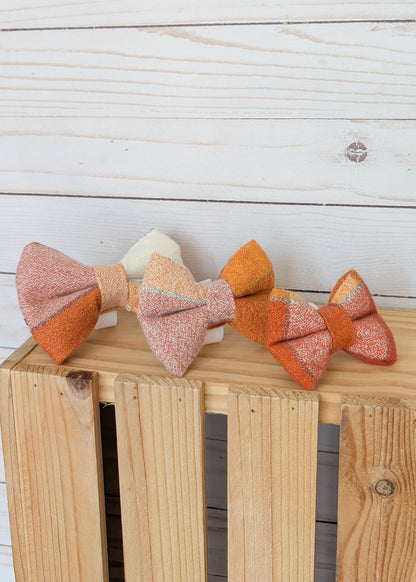 Three handmade fabric bow ties in warm autumn and pastel tones displayed on a wooden crate against a white wood plank background.