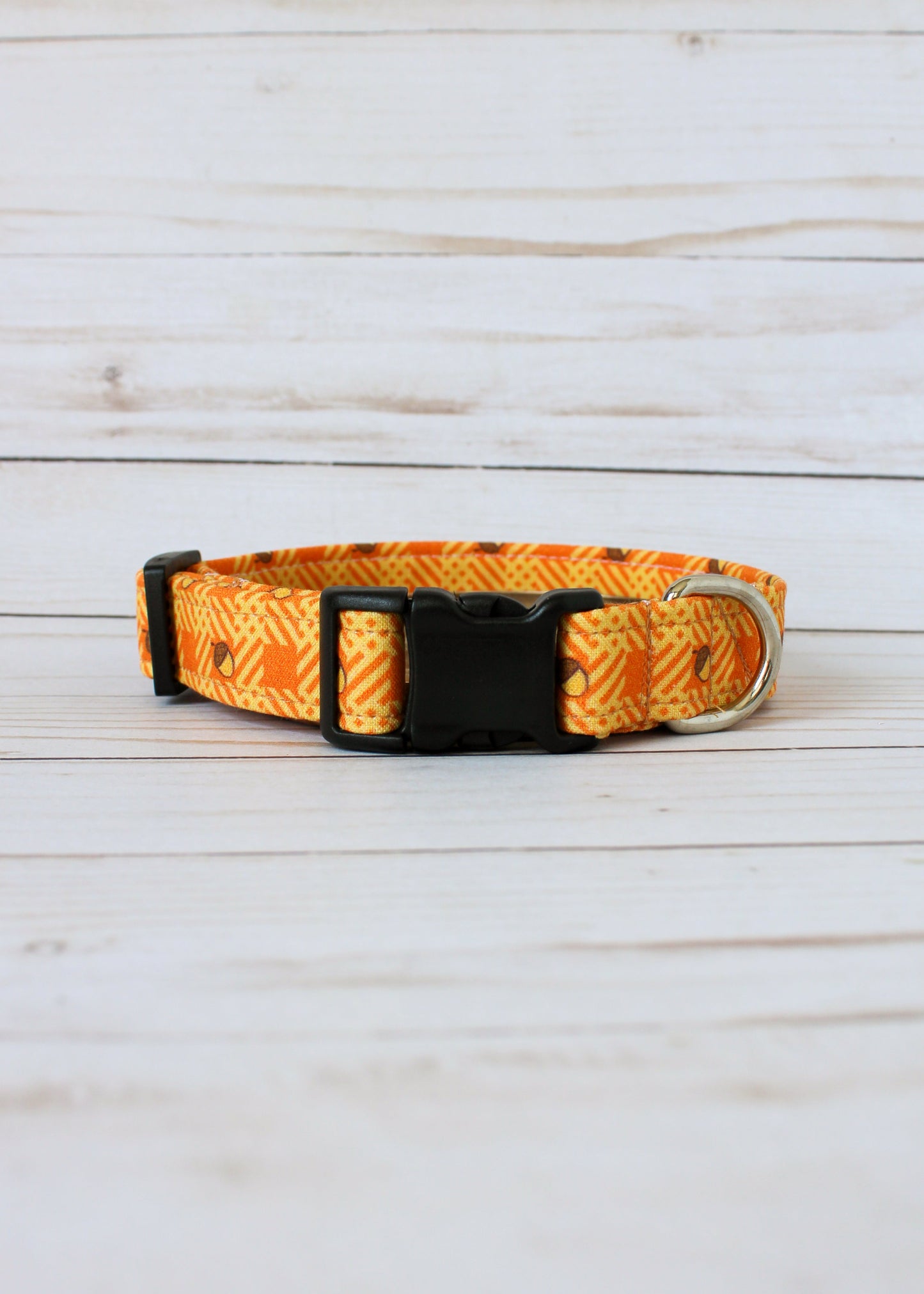 Dog collar with orange and yellow pattern with acorns on a light wooden surface