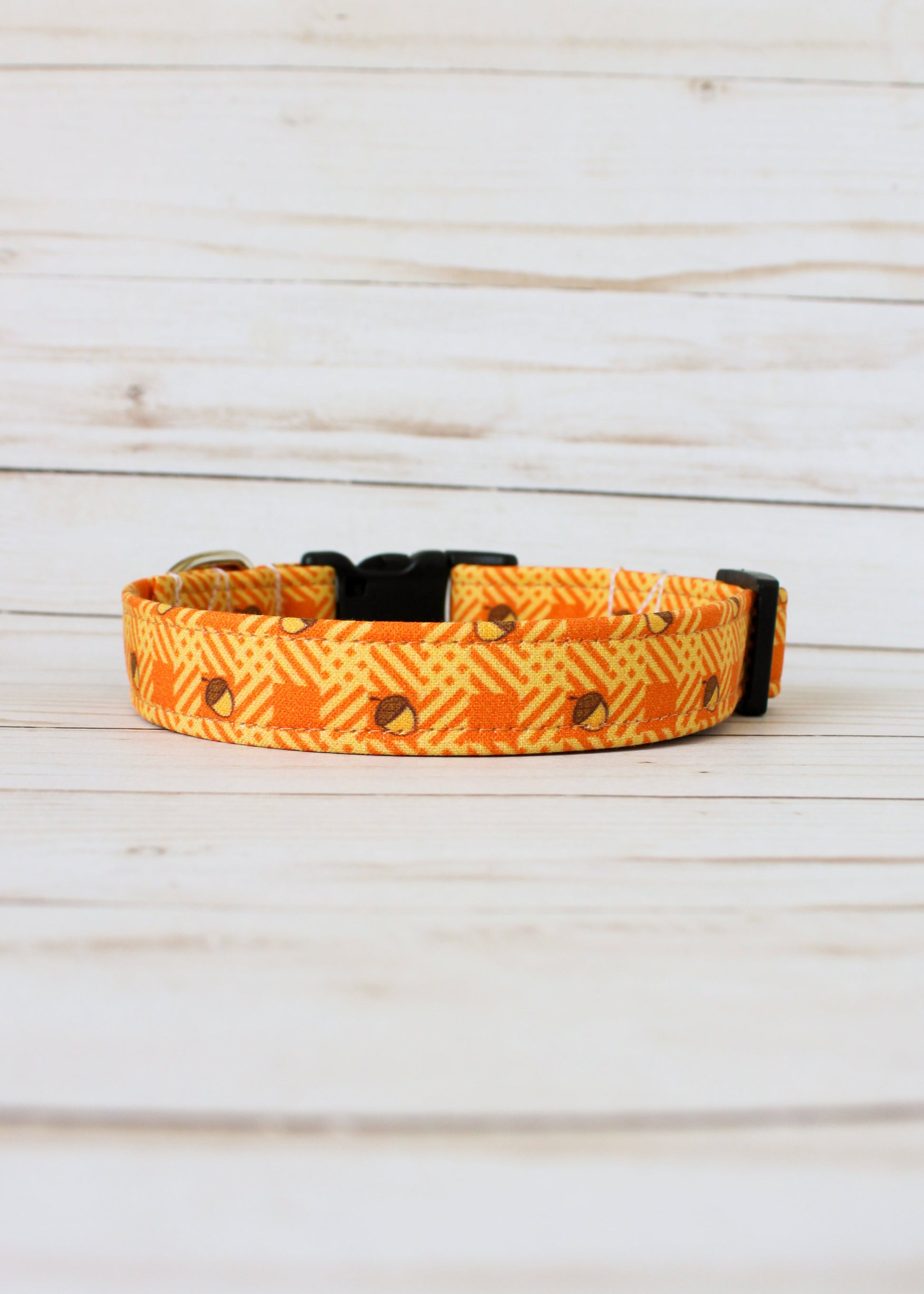 Dog collar with orange and yellow pattern with acorns on a light wooden surface