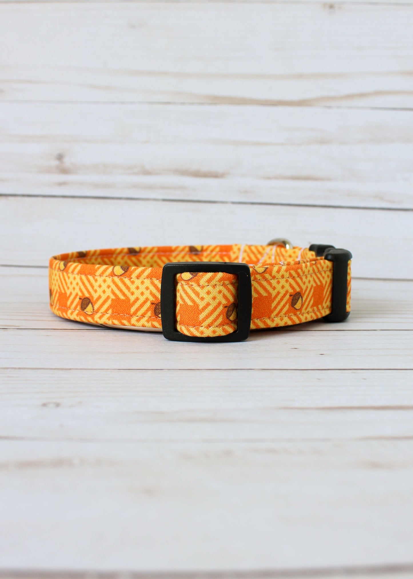 Dog collar with orange and yellow pattern with acorns on a light wooden surface