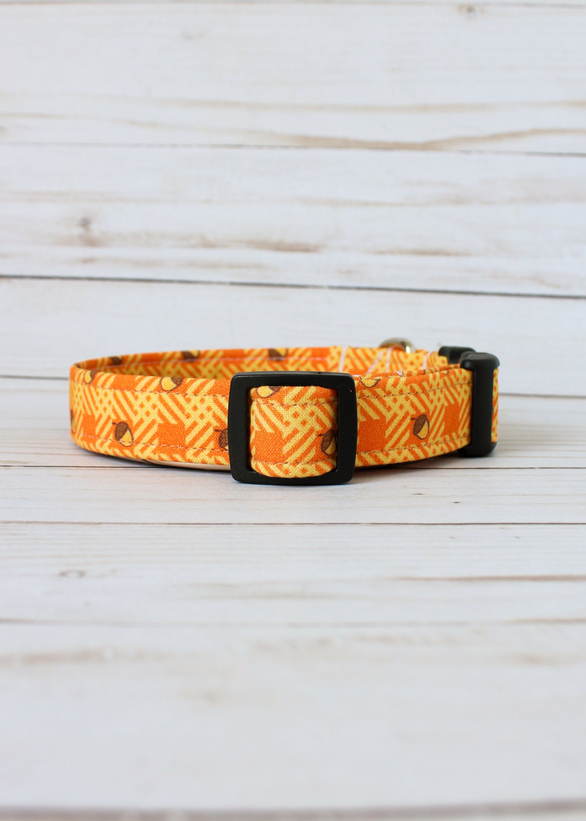 Dog collar with orange and yellow pattern with acorns on a light wooden surface