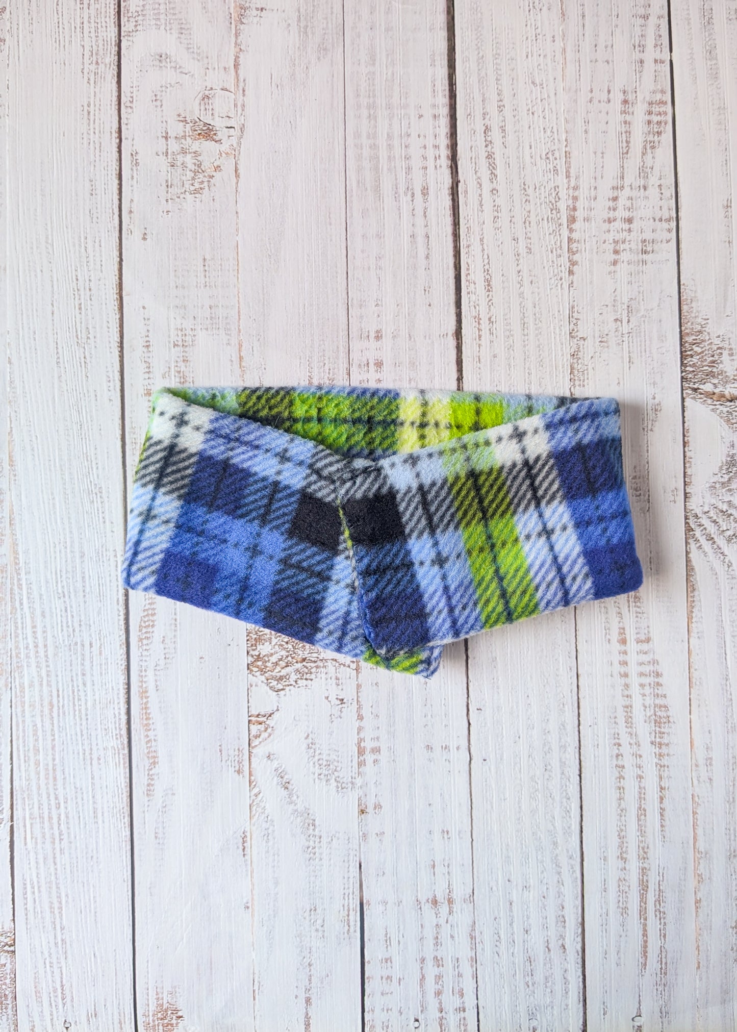 Blue, lime, white, black plaid fleece scarf on a wooden background