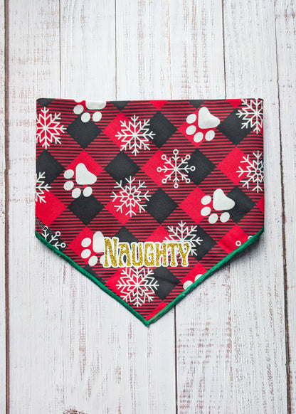 Red and black buffalo plaid bandana with green hem edge, white snowflake and paw print pattern and "naughty" as a central text in gold shimmer with white outline
