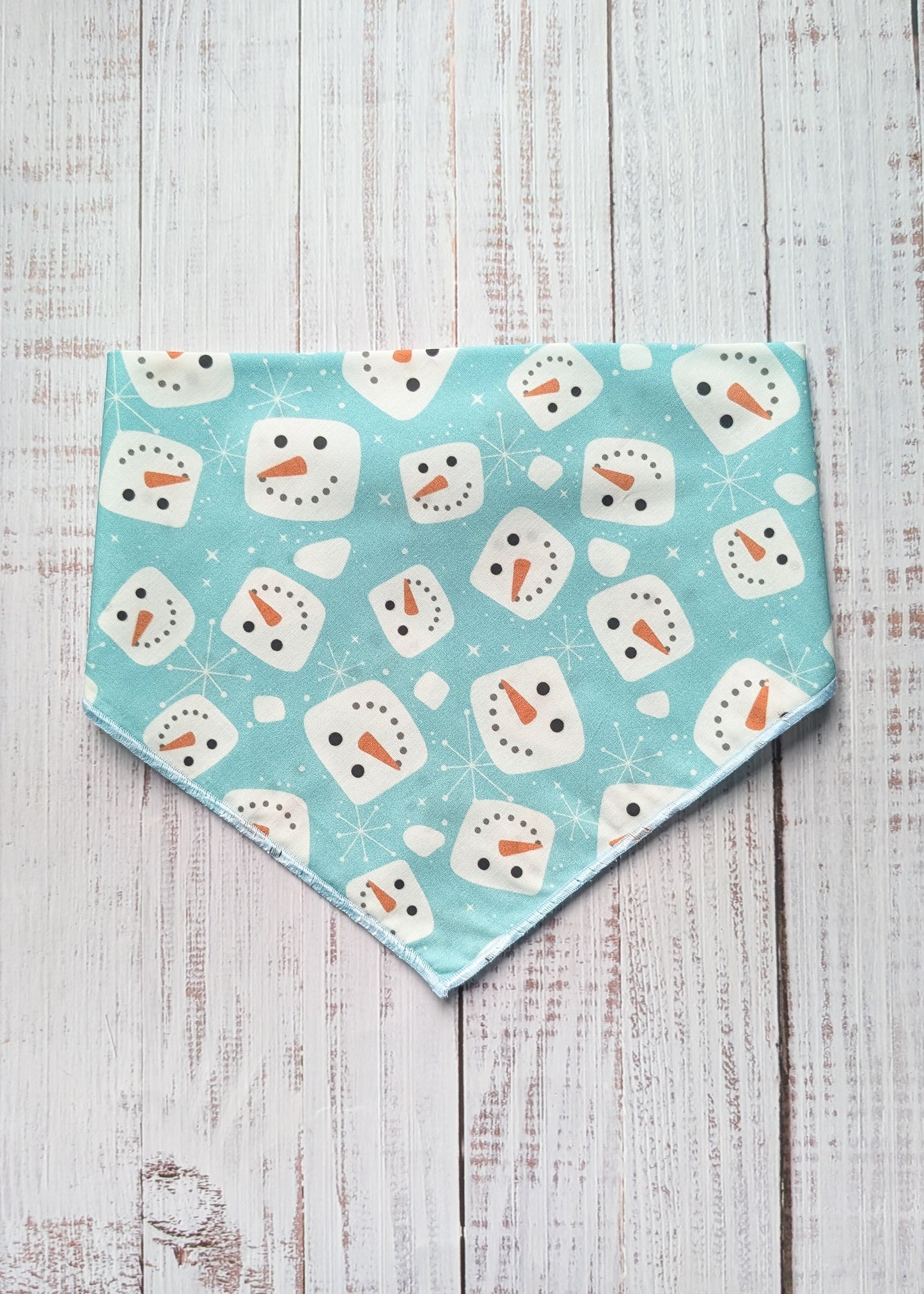 Fabric with snowman pattern on a light blue background, placed on a wooden surface.